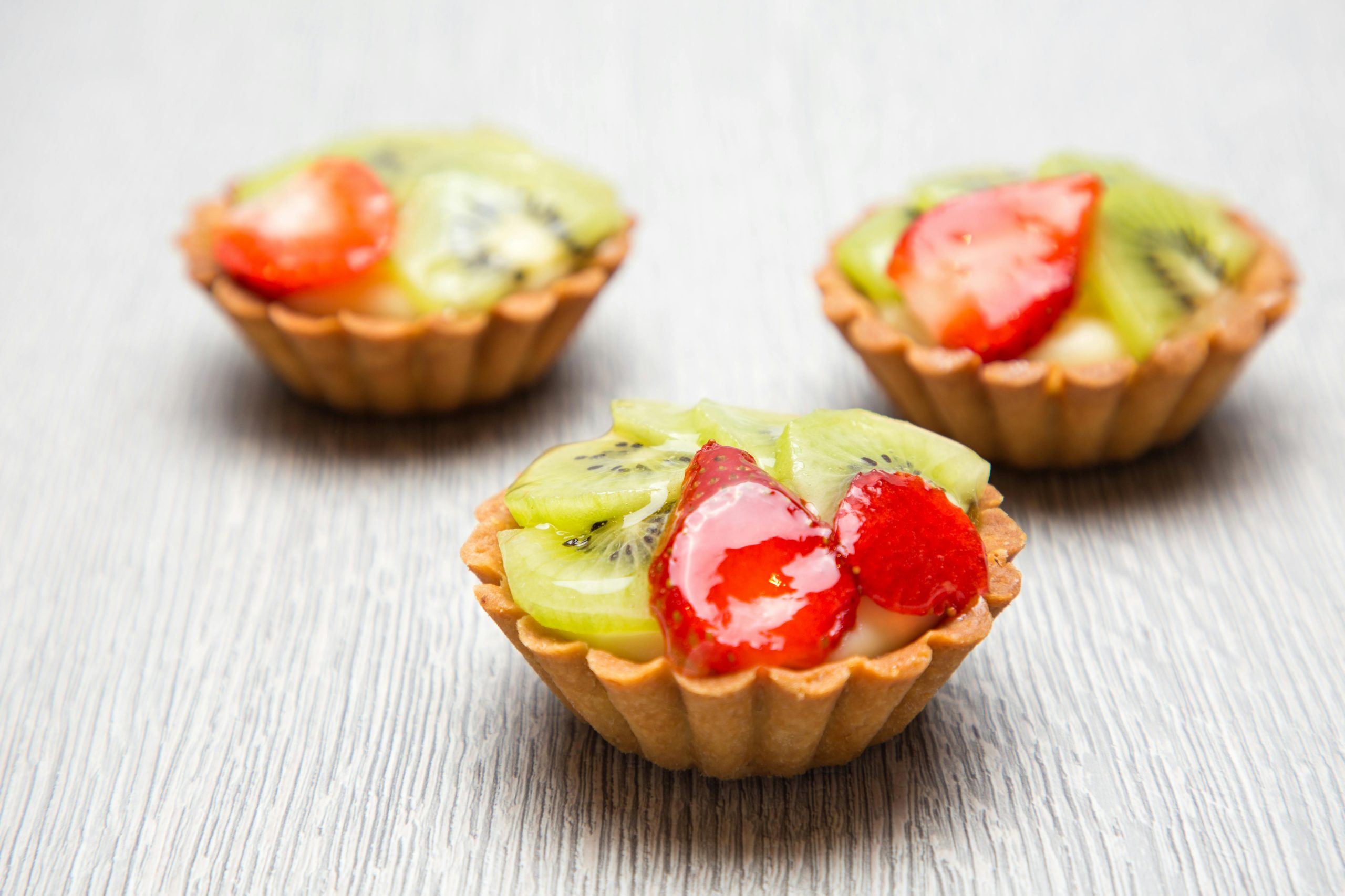 Close-up of three fresh fruit tarts topped with kiwi and strawberry slices on a wooden table.