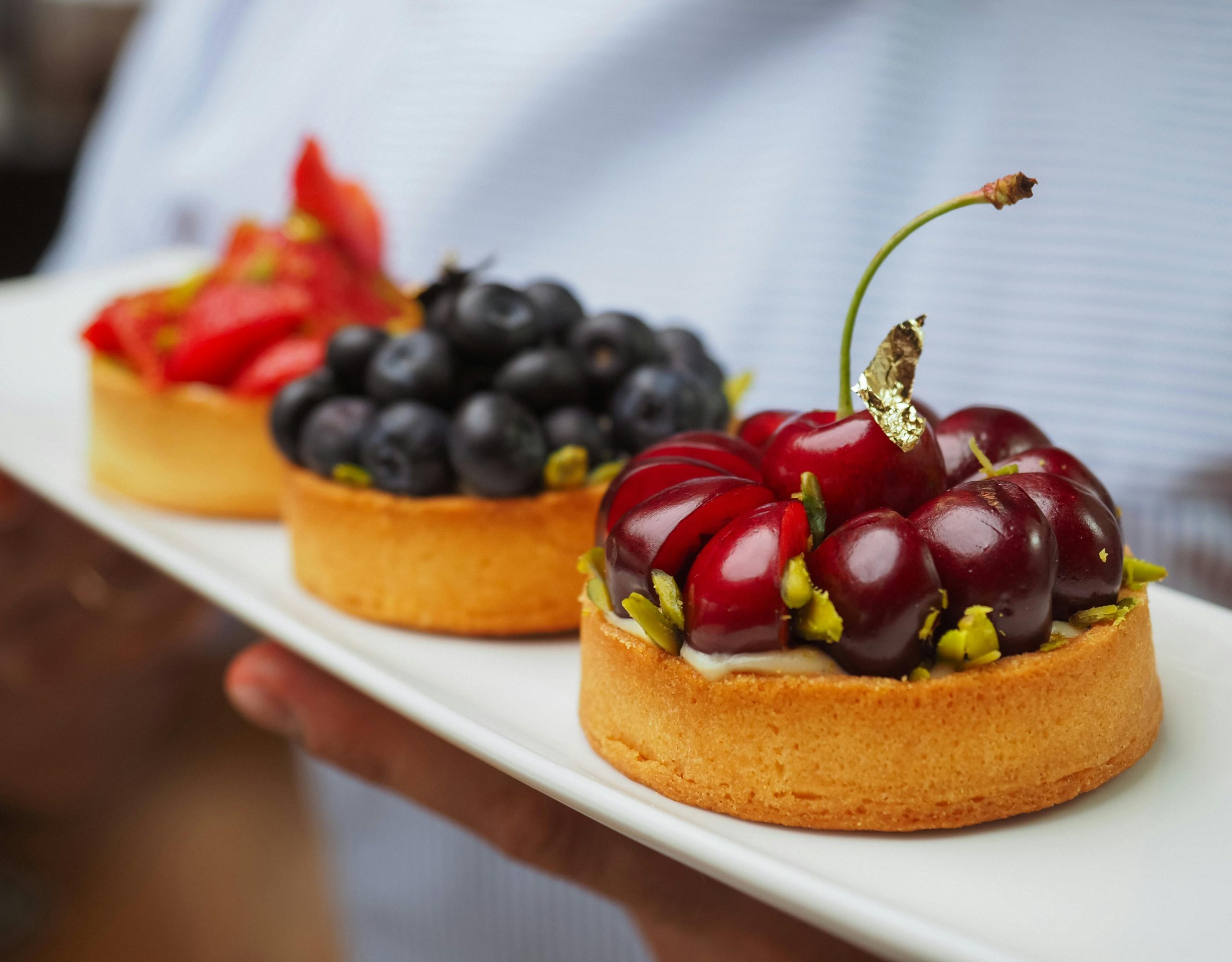 Close-up of assorted fruit tarts with cherries and blueberries on a serving plate.