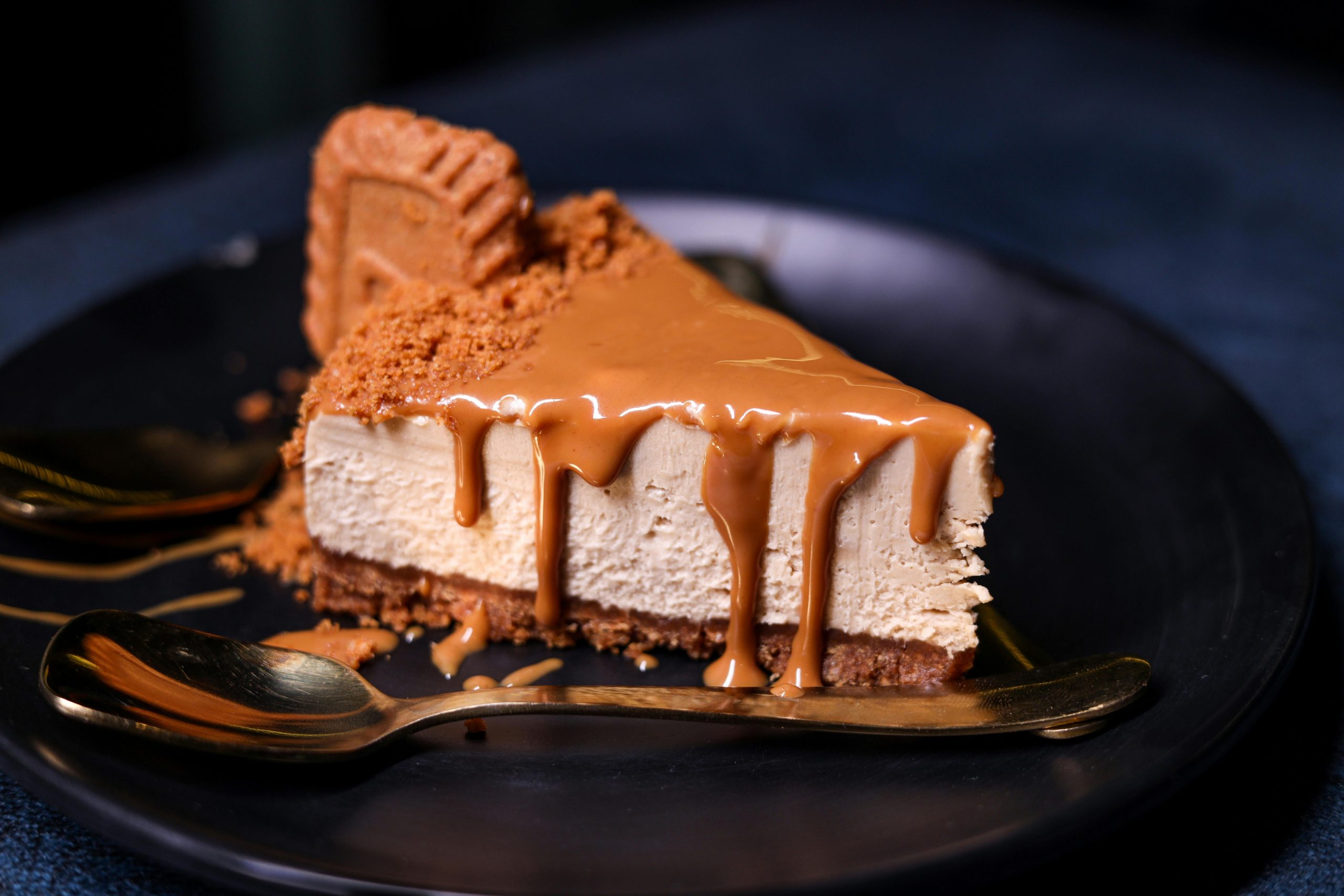 A mouthwatering slice of cheesecake with caramel drizzle on a dark plate, perfect for dessert lovers.