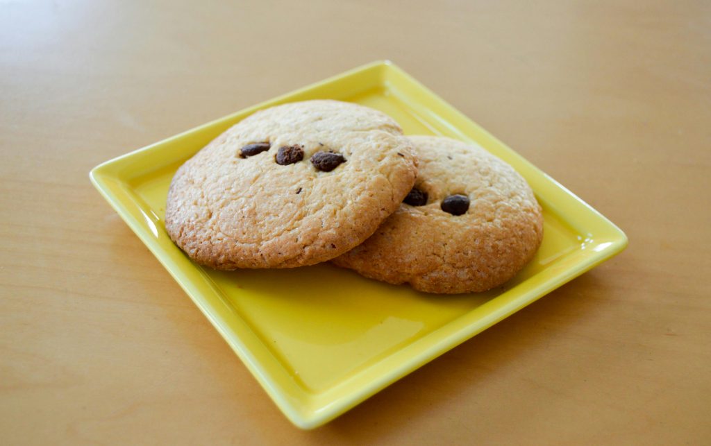 Two freshly baked chocolate chip cookies served on a yellow plate.
