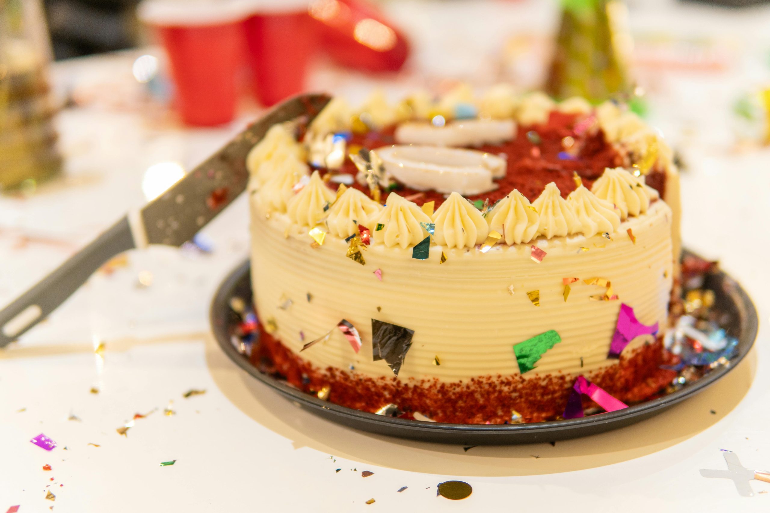 Red velvet cake on a party table with confetti and a serving knife.